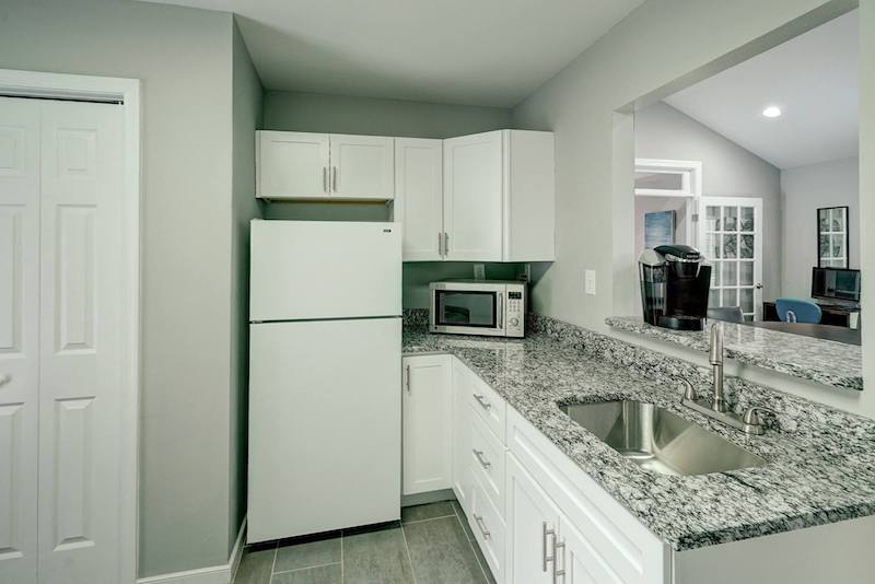 Refrigerator, microwave, and sink in a kitchen with white cabinets and granite countertops