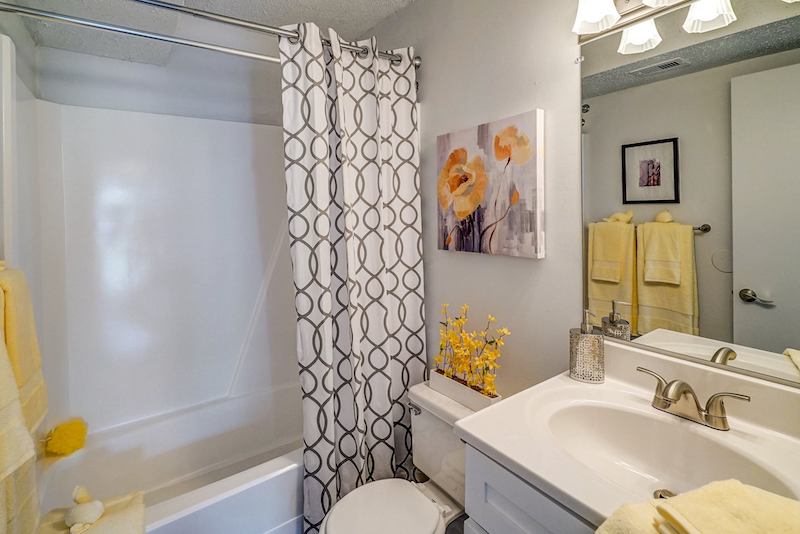 Full bathroom with white counter, shower, and a painting of an orange flower