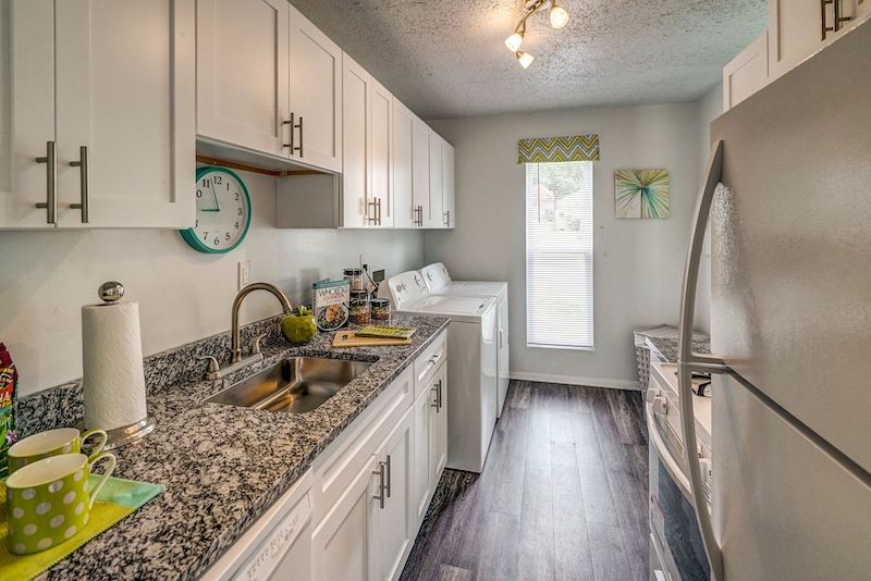 Shotgun-style kitchen with granite countertops, white cabinetry, and a full-size washer and dryer