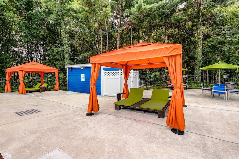 Cement sundeck with two cabanas surrounded by tall, lush trees