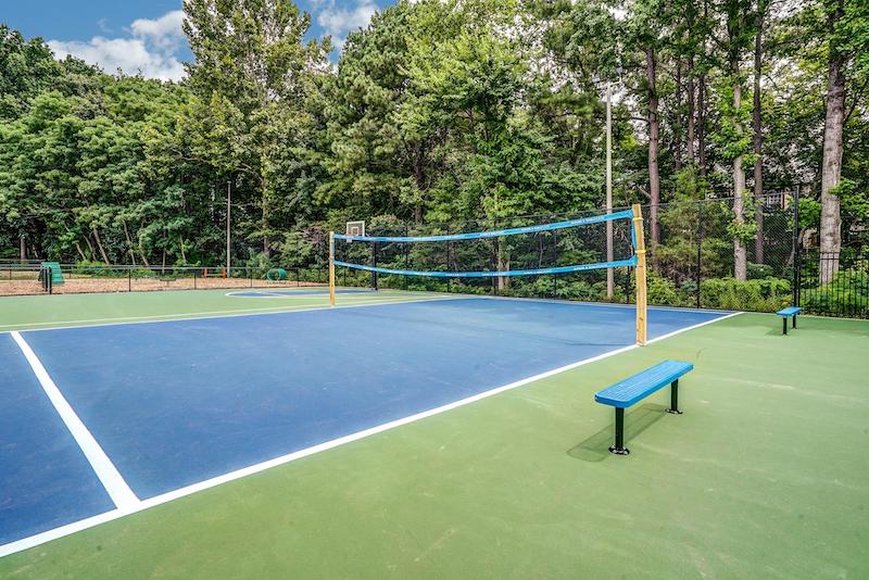 Volleyball court with tall green trees and a basketball court in the near background